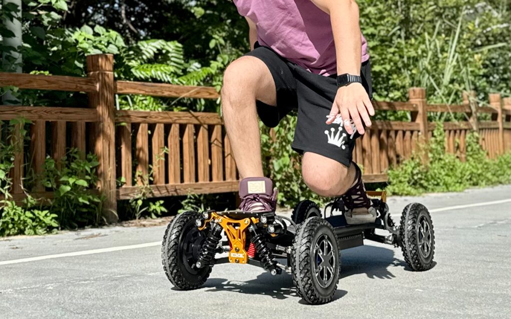 Ecomobl M24 PRO electric skateboard with orange suspension, riding on paved path. All terrain electric skateboard