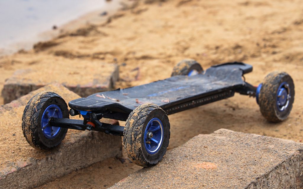 Ecomobl ET Pro 2WD all-terrain electric skateboard on sand, featuring large wheels and blue hubs.