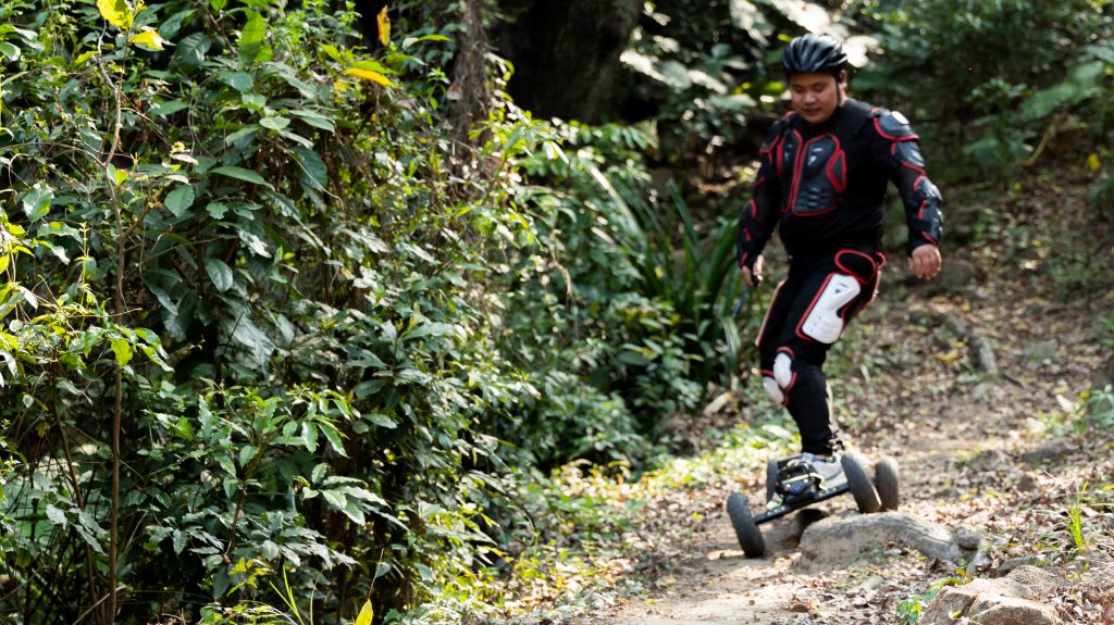 Person riding an electric skateboard on a forest trail.