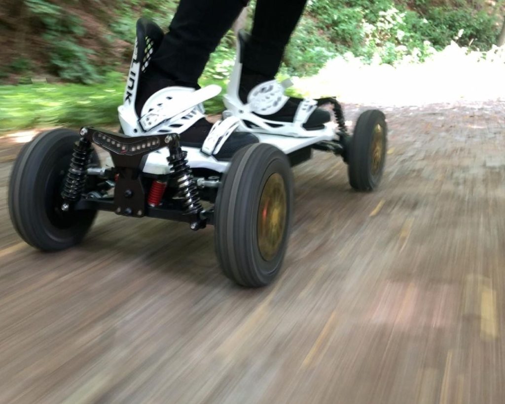 Close-up of feet riding an electric skateboard on a paved path.