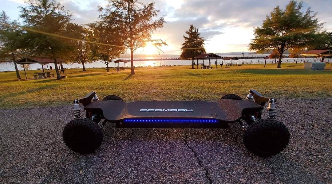 Electric skateboard parked at sunset near a lake.