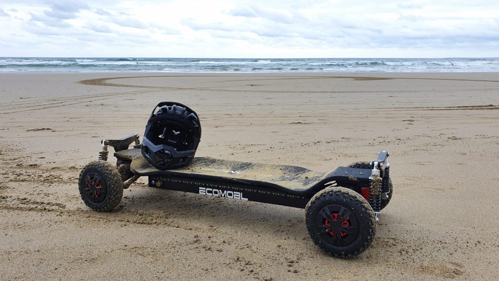 Electric skateboard with a helmet on a sandy beach.