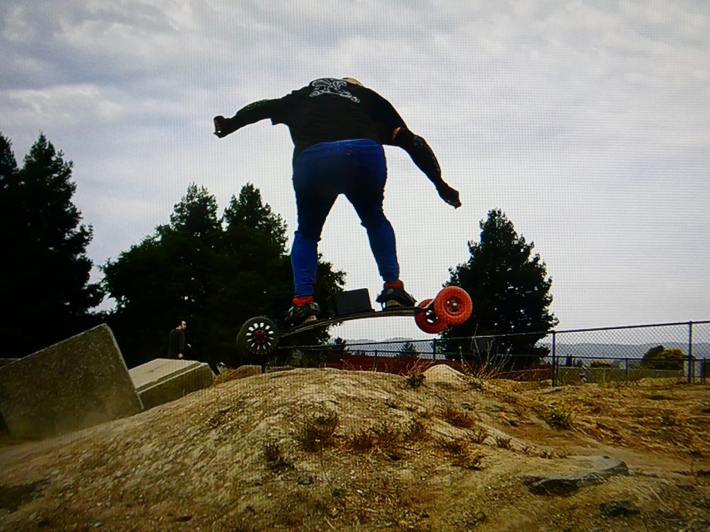 Person performing a jump on an electric skateboard over a dirt mound.