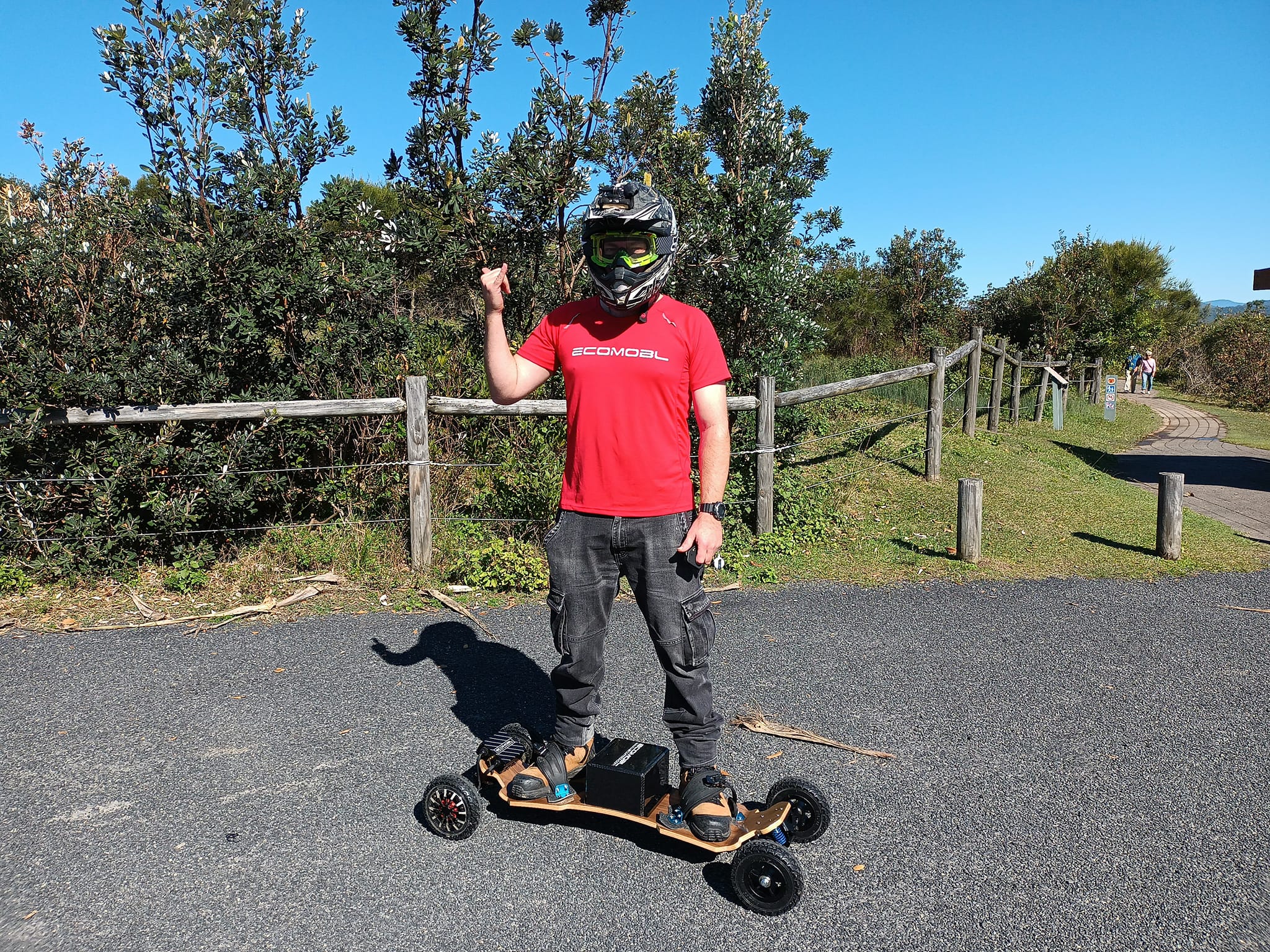 Person standing on an electric skateboard wearing a helmet, with trees in the background.