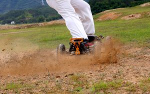 Person riding an electric skateboard on a dirt path, kicking up dust.